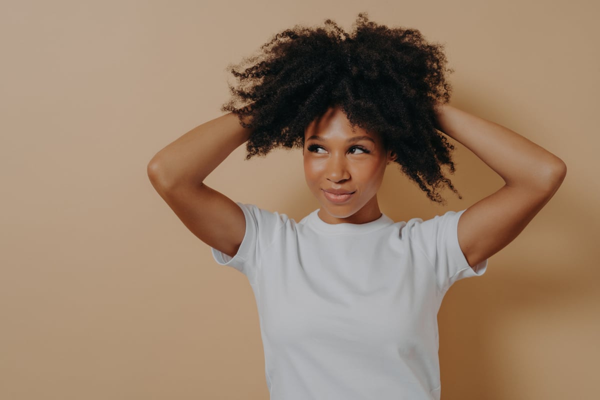 Young Attractive  African Woman Touching with Hands Curly Hair, Isolated on Beige Background